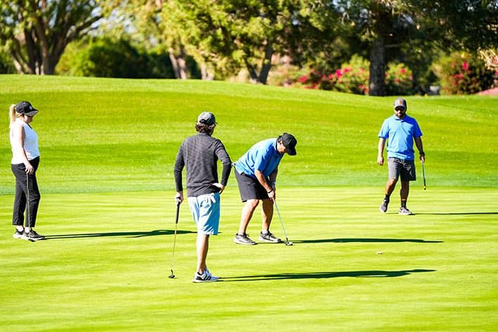 Four people are on a golf course; one is putting while the others watch during the SITE SoCal Holiday Event Golf Tournament.