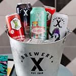 A metal bucket labeled "Brewery X" holds assorted colorful cans of beer surrounded by ice.