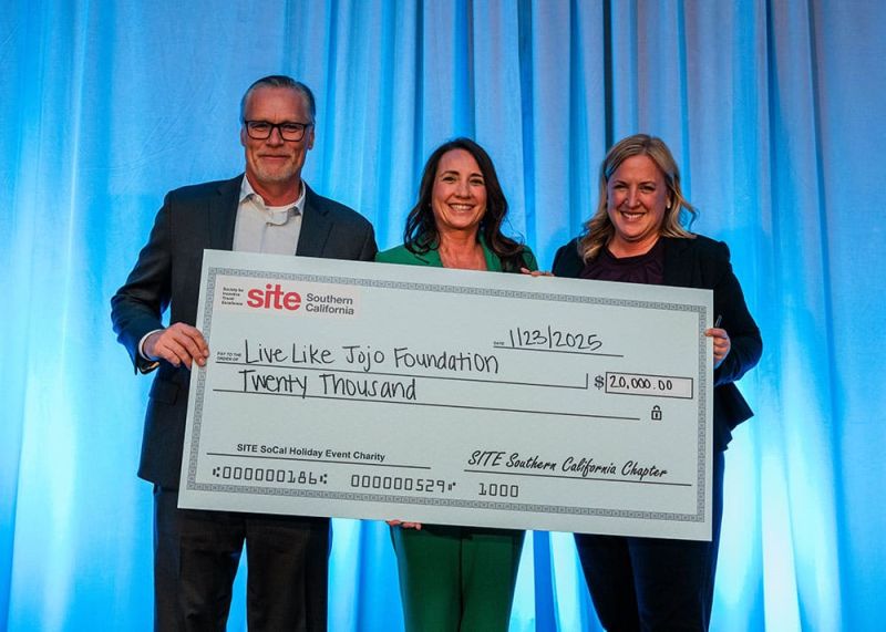 Three people standing with a large check for $20,000 made out to the Live Like Jojo Foundation against a blue curtain background.