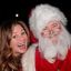 A woman smiling widely poses next to a person dressed as Santa Claus.