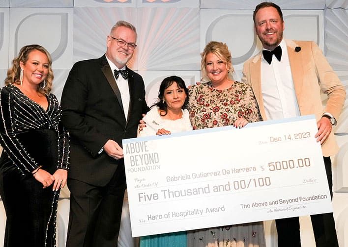 Group of five people standing, with one person holding an oversized check for $5000 donation to the Above and Beyond Foundation.